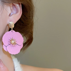 Détail de boucle d'oreille fleur rose avec pétales texturés et perle portée sur l'oreille