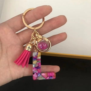 Detail of a resin letter L keychain with colorful stones, pink tassel, and gold hardware