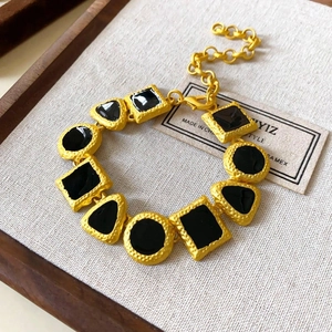 Detail of gold geometric link bracelet with black inlay on a rustic wooden tray