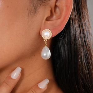Elegant gold drop earrings with round and teardrop pearls worn by a model in close-up view