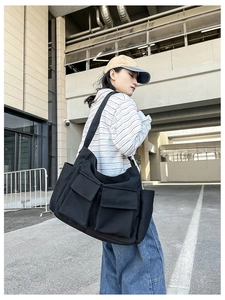 Black canvas tote bag detail showing large front pockets and wide shoulder strap
