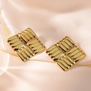 Macro shot of gold square stud earrings with vertical textured stripes on silk fabric