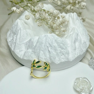 Elegant gold-plated copper leaf ring with green enamel finish set against floral decor