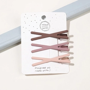 Three matte X-shaped hair clips in brown and pink hues displayed on white card
