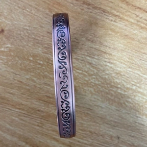 Macro detail of antique copper magnetic bracelet featuring engraved spiral patterns on wood