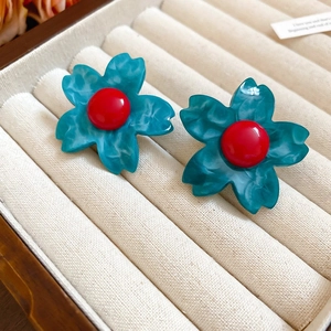 Detailed close-up of teal resin flower earrings with red centers in a velvet gift box