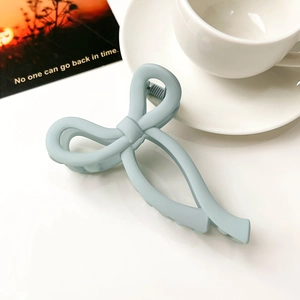 Detail of matte light blue bow-shaped hair claw clip on a minimalist aesthetic background