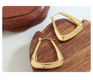Macro shot of U-shaped gold earrings on wood texture showcasing 18k plated finish