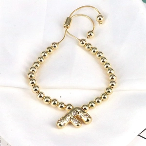 Detailed shot of golden bead bracelet with zircon-studded letter F charm and adjustable cord