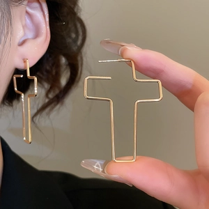 Gros plan détaillé de boucles d'oreilles croix dorées montrant texture et dimensions