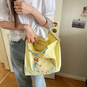 Détail d'un sac cabas brodé jaune clair avec des poignées à carreaux bleus et liseré