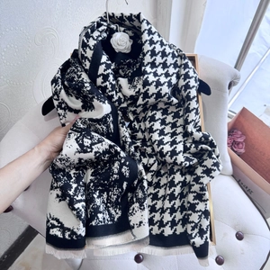 Detail showing monochrome houndstooth scarf texture and fringe hanging from a hand