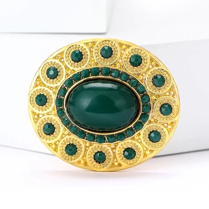 Close-up of vintage oval brooch with dark green crystals and intricate gold metalwork