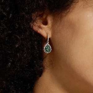 Pear-shaped green moss agate earrings with silver diamond halo on a model's ear