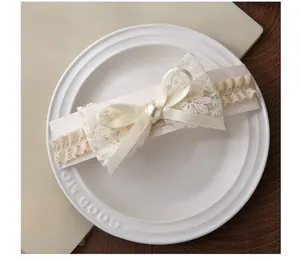 Détail d'un bandeau bébé en dentelle crème avec nœud en ruban et perle sur une assiette
