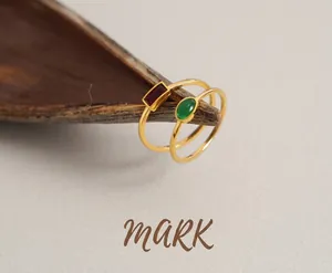 Close-up of minimalist gold titanium rings with rectangular red and oval green zircons
