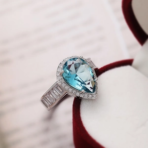 Macro detail of pear-cut light blue gemstone ring with pave diamonds on white gold band