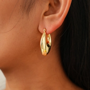 Close-up of chunky gold-toned hoop earring showing polished mirror-like metal finish