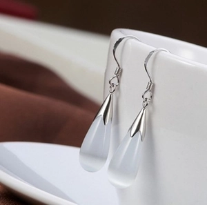 Elegant silver-plated teardrop earrings with white cat-eye stone on a white ceramic cup