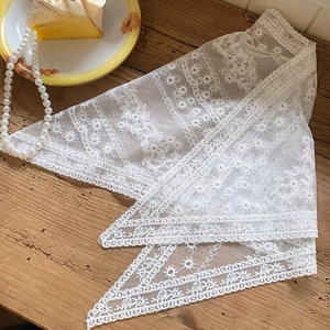 Close-up of white floral lace triangle scarf on wood table with pearls and dessert
