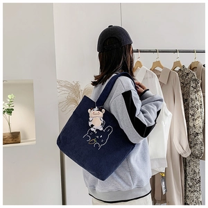 Blue corduroy tote bag with rabbit embroidery and cow plush charm shown on shoulder