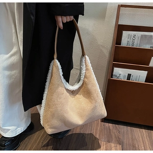 Detail of suede tote bag with white plush trim held by a model in an indoor setting