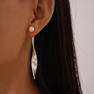 Close-up of elegant long twist metal earring with pearl stud worn by model