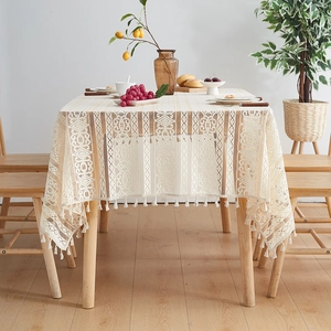 Beige lace tablecloth with hollow patterns and tassels on a wooden dining table