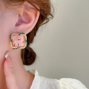 Gros plan d'une boucle d'oreille carrée en résine rose avec bord doré et détails verts