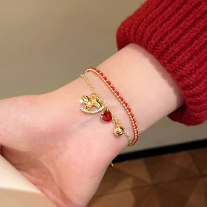 Close-up of red rope bracelet with gold pony pendant worn with red knit sweater