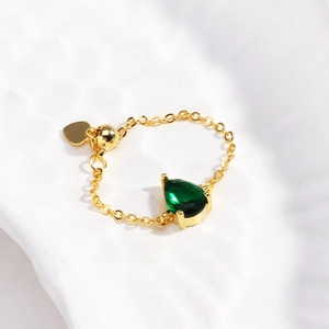 Détail d'une bague chaîne ajustable dorée avec pierre verte poire et breloque cœur