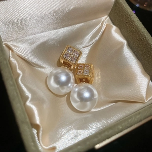 Macro detail of gold square zircon earrings with large white pearl drop on silk