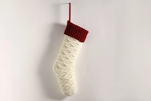 Detail of cream fish-scale knit Christmas stocking with a red ribbed cuff and hanging loop