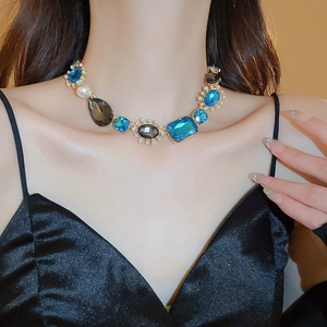 Close-up of a vintage necklace with blue gemstones and pearls on a model wearing black V-neck