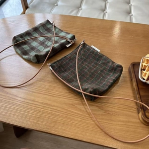 Detail showing vintage plaid wool crossbody phone bags with thin shoulder straps on a wood table