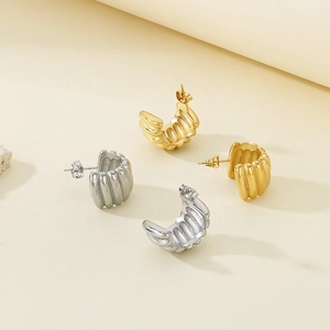 Detail of gold and silver C-shaped ribbed earrings with polished stainless steel texture