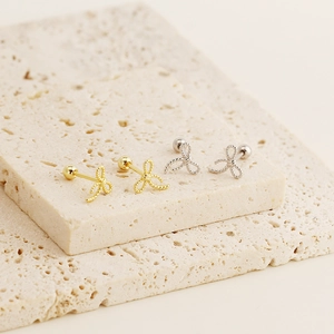 Macro shot of gold and silver sterling silver bow earrings on a beige stone surface