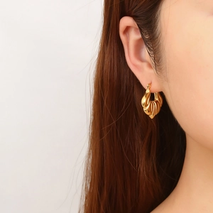 Detail of vintage gold C-shape hoop earrings with textured seashell pattern on model