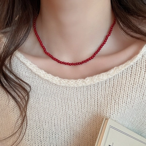 Close-up of minimalist red glass beaded necklace worn over a white knit sweater