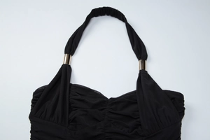 Close-up of black backless halter dress showing ruched mesh fabric and gold hardware