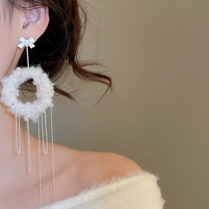Detail of plush white circular earrings with silver tassels and a delicate bow knot