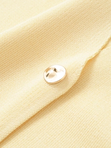 Detailed view of yellow knit fabric texture with a polished gold round metal button