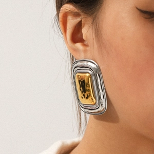 Close-up of oversized rectangular gold and silver geometric earrings on a model