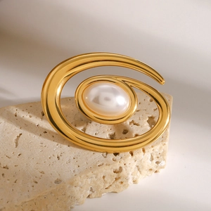 Detailed view of the spiral 18k gold-plated pearl brooch on a minimalist stone base