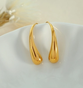 Close-up of gold teardrop earrings in a white ceramic dish with a floral background