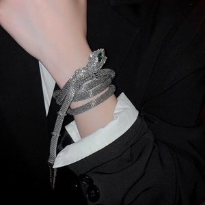 Detail of silver snake-shaped wrap bracelet encrusted with white rhinestones and green eyes