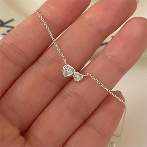 Macro shot of minimalist 925 silver necklace featuring two clear heart-shaped zircon pendants
