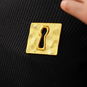 Detailed macro view of a vintage hammered gold square brooch with a keyhole design on black fabric