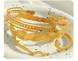 Detailed view of layered 18K gold plated Cuban chain bracelets and vintage textured bangles