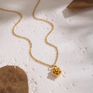 Elegant gold camellia flower pendant necklace on minimalist stone background